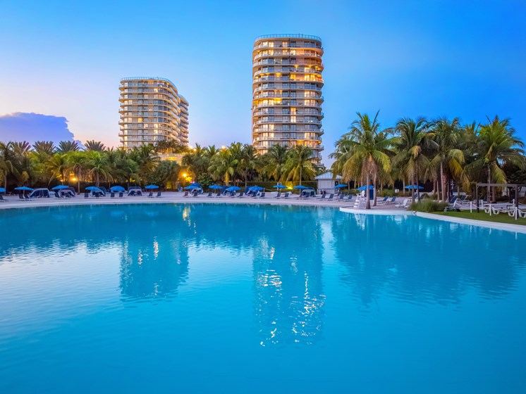 A swimming pool in front of two tall buildings with palm trees around it.